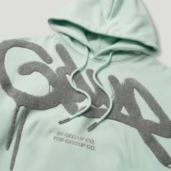 Close-up of the Geedup Handstyle logo on the teal cropped hoodie.