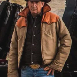 Kevin Costner wearing the Yellowstone Season 3 John Dutton jacket, a rugged brown and tan Western-style coat.