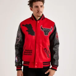 A man wearing a red and black Chicago Bulls varsity jacket with embroidered team logos and patches on the front and sleeves.
