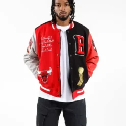 A man wearing a Men's Pro Standard NBA Chicago Bulls Varsity Jacket with a bold red and black design, featuring embroidered Bulls logos, championship trophy patch, and stylish detailing.