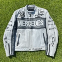 A front view of the Mercedes Benz Racing Leather Jacket, featuring a silver-gray leather body with black detailing, multiple sponsor patches, and a bold "Mercedes" logo across the chest.