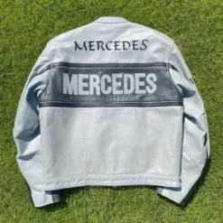 A back view of the Mercedes Benz Racing Leather Jacket, showcasing the "Mercedes" logo across a black leather stripe, set against a silver-gray leather body.