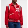 A person wearing the Mother The Team Spirit Varsity Jacket in red, featuring a bold letter "M" patch on the chest and striped detailing.
