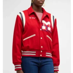 A person wearing the Mother The Team Spirit Varsity Jacket in red, featuring a bold letter "M" patch on the chest and striped detailing.