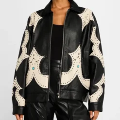 A model wearing the Mother The Zip It Studded Leather Jacket in black with beige Western-inspired detailing, silver studs, and turquoise embellishments. The jacket has a relaxed fit, a zip closure, and a structured collar.