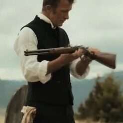 A man wearing the Murder at Yellowstone City 2022 Thaddeus Murphy Vest, a black button-up vest over a white long-sleeve shirt, in an old Western setting while holding and inspecting a rifle.