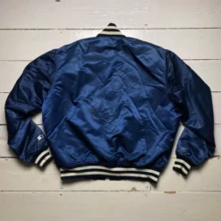 A navy blue New York Yankees bomber varsity jacket with striped ribbed collar, cuffs, and waistband, displayed on a wooden floor.