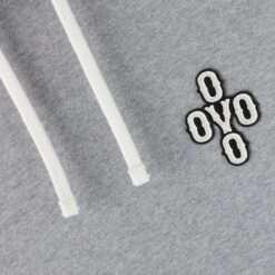 Close-up of the OVO Pom Pom Grey Hoodie logo embroidery with textured detailing.
