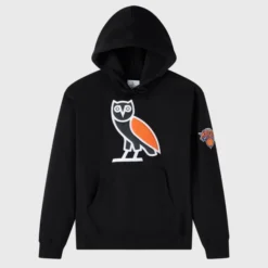Black OVO x NBA New York Knicks hoodie with an oversized OVO owl logo in black, white, and orange on the chest, and a New York Knicks patch on the sleeve.