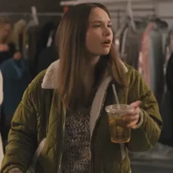 Lucy wearing a green quilted puffer jacket with a pink ruffled dress and a furry bucket hat in a wooden-paneled elevator.