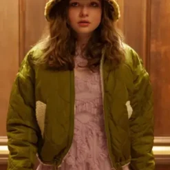 Lucy in a green quilted puffer jacket with white shearling lining, holding a drink in a busy store setting.