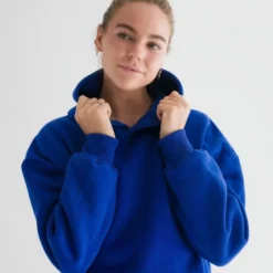 Woman in a royal blue hoodie with a white palm tree logo on the chest, looking stylish and cozy.
