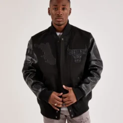 A male model wearing the Pro Standard Chicago Bulls Varsity Black Jacket, featuring embroidered Bulls logo and Chicago map details on the front.