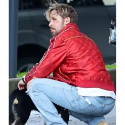 Ryan Gosling crouching while wearing a red leather jacket with white piping on the back.
