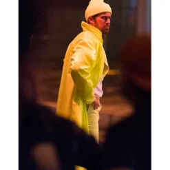 Side view of Ryan Gosling wearing a yellow long coat with a matching beanie, creating a bold and stylish cinematic look.