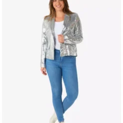 A woman wearing a sequined silver blazer over a white top and blue jeans, standing and smiling.
