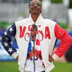 Snoop Dogg wearing a U.S. Olympic 2024 bomber jacket with red, white, and blue patriotic design.