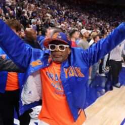 Spike Lee wears a New York Knicks jacket at Caesars Arena during the NBA Playoffs, showcasing a bold, team-themed design with vibrant colors and the iconic Knicks logo, highlighting his passionate fan spirit.